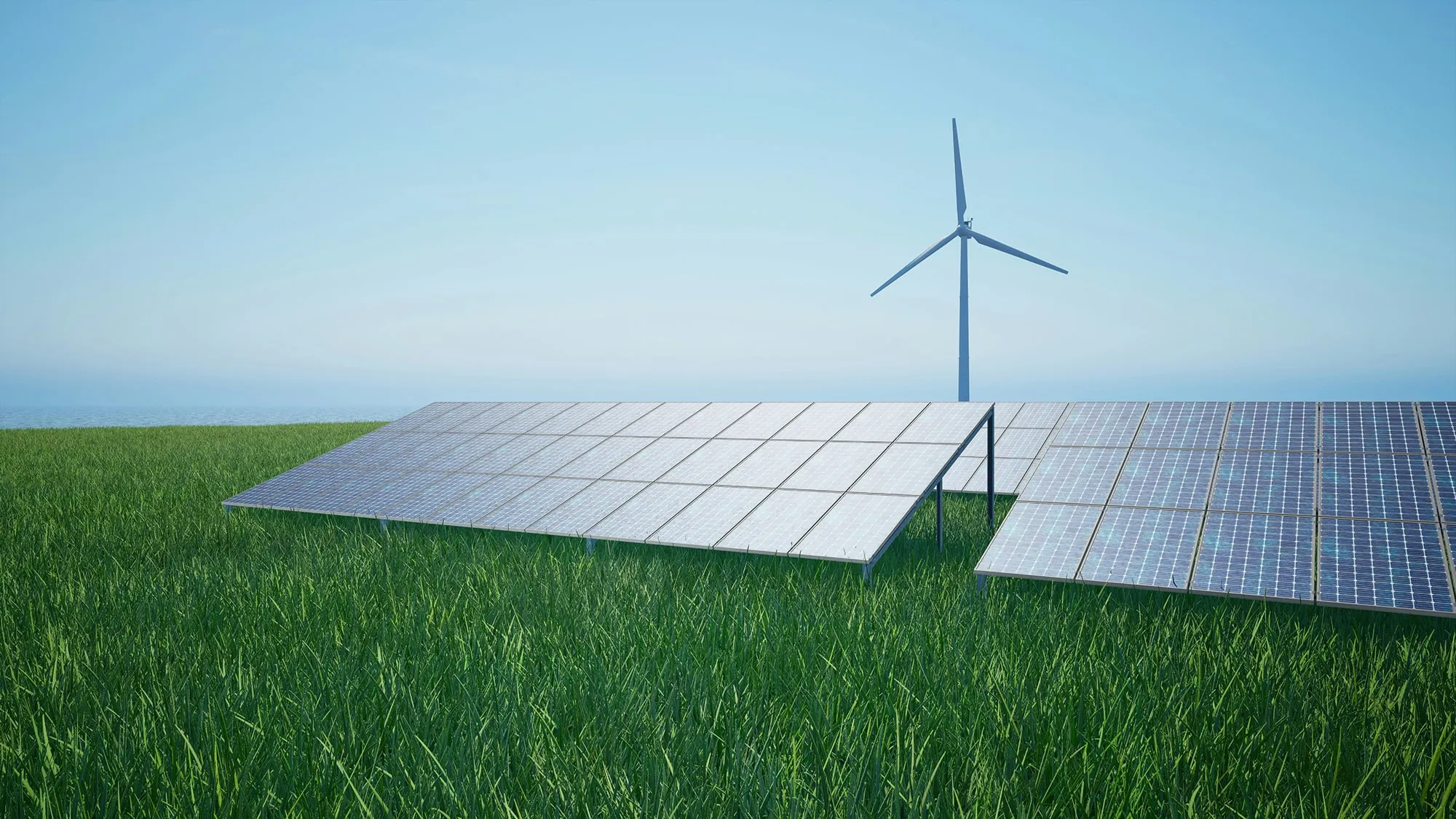 Solar panels installed on green grass with a wind turbine in the background under a clear blue sky.